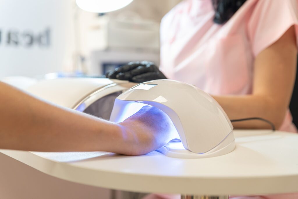 Woman holds fresh manicure in the UV LED nail lamp